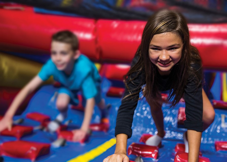 Pump It Up arena space for private parties with kids climbing a large inflatable attraction.